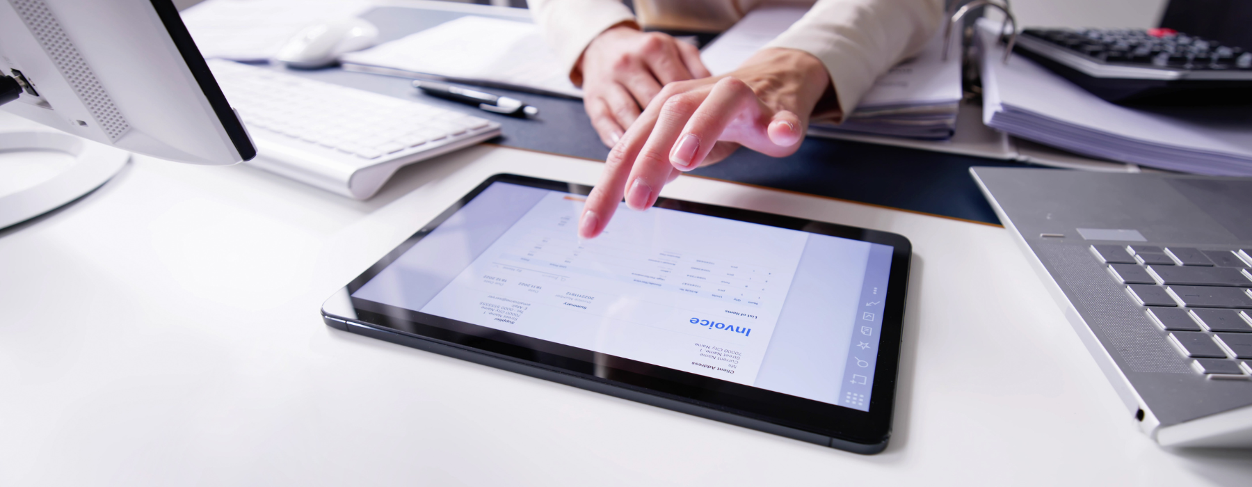 A close-up of a professional’s hands using a tablet or computer with visible invoice or payment data on the screen