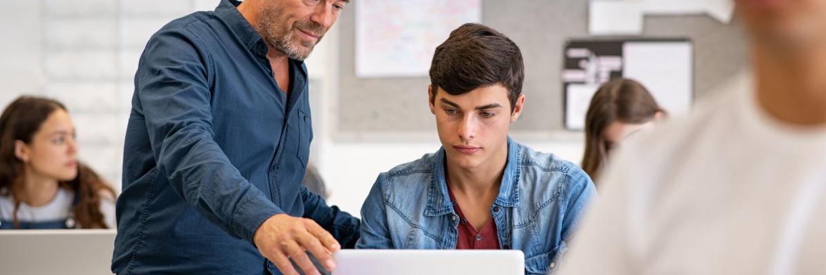 Teacher assisting student with laptop in classroom 